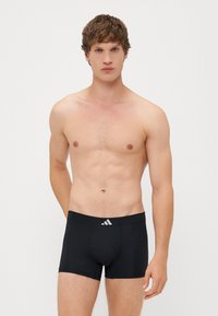 Črne bokserice iz elastičnega materiala, s prilagojenim krojem in izstopajočim Adidasovim logotipom na pasu.