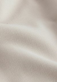 Beige tyg med en mjuk, slät textur som har ett fint ribbat mönster. Materialet verkar lätt och flexibelt.