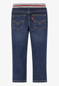 Pantalon en denim bleu foncé avec une ceinture élastique grise ornée de rayures rouges. Deux poches arrière avec des coutures jaunes et une étiquette de marque visible.