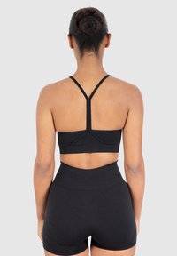 Sujetador deportivo negro con tirantes finos y una banda inferior ancha, combinado con pantalones cortos negros de cintura alta, que presentan un diseño sin costuras y tela elástica.