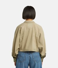 Giacca corta beige con una vestibilità rilassata, caratterizzata da maniche lunghe e una texture liscia. La giacca include cuciture sulle spalle e tasche laterali.