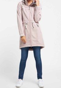Light pink long coat with a zip front, adjustable hood, and drawstring waist; paired with blue jeans and white sneakers. Smooth texture.
