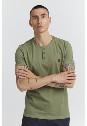 Olivengrønn bomulls t-skjorte med korte ermer, rund hals og tre knapper foran; har en liten logo på brystet.