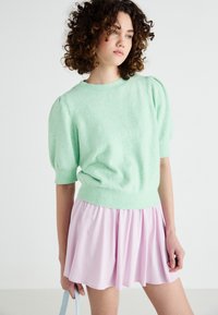 Mintgrön tröja med kort puffärm, bärs med en ljusrosa utsvängd kjol. Mjuk textur, klassisk rund halsringning och subtila ribbade detaljer.