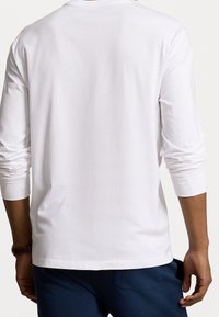 Maglietta bianca a maniche lunghe con scollatura rotonda, realizzata in morbido cotone, con polsini aderenti, abbinata a pantaloni blu navy. Design semplice, senza motivi.