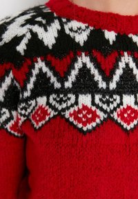 Rode gebreide trui met zwarte, witte en rode geometrische patronen bij de halslijn. De textuur lijkt zacht en dik, geschikt voor warmte.