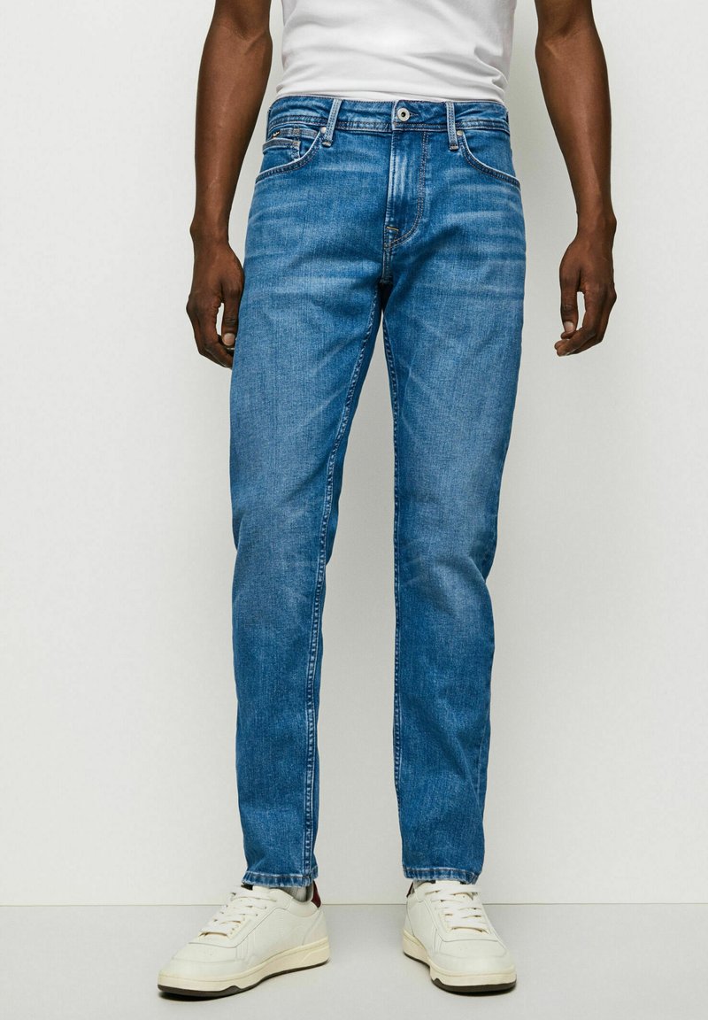 Jeans din denim albastru cu un design drept al piciorului, cinci buzunare și un model discret de degrade, asortați cu adidași albi.