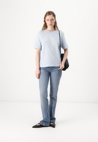 Light blue cotton t-shirt with short sleeves and a printed logo, paired with light blue flared jeans and black pointed flats.