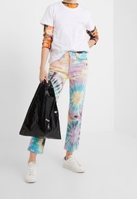 Kleurrijke tie-dye jeans in pastelkleuren van blauw, roze en geel, gecombineerd met een eenvoudig wit t-shirt en een zwarte tote tas. Witte sneakers.