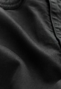 Black fabric with a smooth texture, featuring subtle folds and reflective qualities, showcasing a matte finish and no visible patterns or hardware.