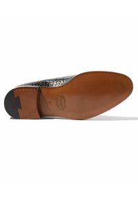 Parte superior de piel con relieve de cocodrilo negro y suela de cuero marrón suave. Presenta una puntera redonda y pequeños acentos metálicos en el tacón.