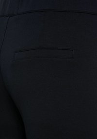 Black leggings with a smooth texture feature a small, flat back pocket. The fabric appears stretchy and form-fitting.