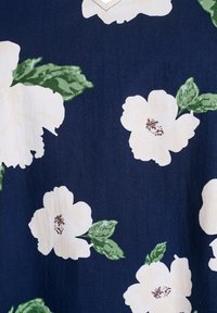 Marineblauer Stoff mit einem floralen Muster, das große weiße Blumen und grüne Blätter zeigt. Weiche Textur, sichtbare Stoffstruktur und leichter Glanz.