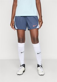 Nike activewear featuring blue shorts with a coral logo, paired with white socks and black cleats, emphasizing athletic design and functionality.