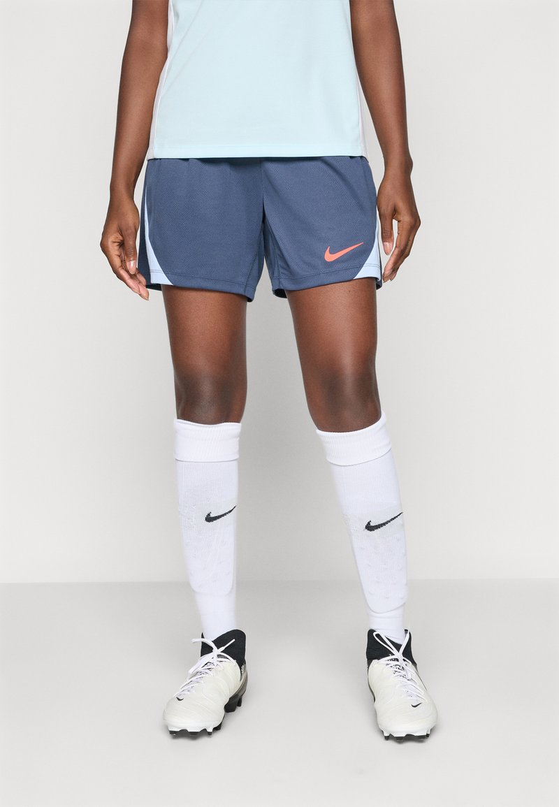 Nike activewear featuring blue shorts with a coral logo, paired with white socks and black cleats, emphasizing athletic design and functionality.