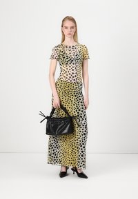 Abito trasparente con stampa leopardata in tonalità gialle e nere, caratterizzato da maniche corte e una silhouette lunga, abbinato a una borsa nera texturizzata.