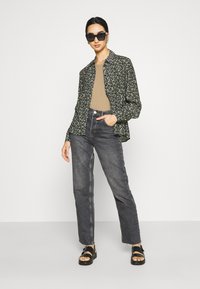 Camicia nera a fantasia floreale sopra una maglietta beige, abbinata a jeans in denim scuro a vita alta e sandali neri con cinturini.