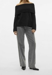 Pull noir à épaules dénudées en maille texturée, accompagné d'un jean gris clair à jambe droite et de bottines noires pointues.