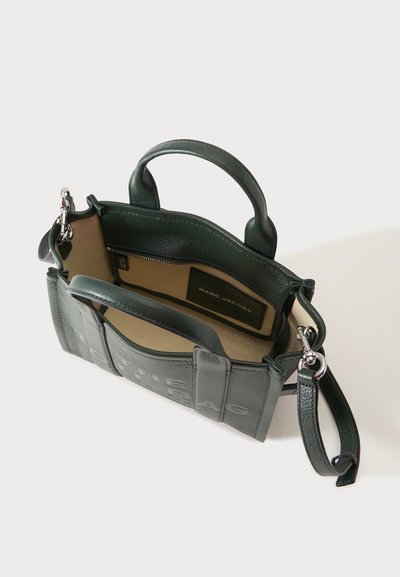 Sac à main en cuir vert Marc Jacobs avec deux poignées, bandoulière détachable, et intérieur beige avec poche zippée et étiquette de marque.