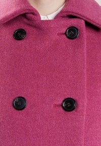 Fuchsia wollen coat met een dubbelbreasted ontwerp, grote zwarte knopen en een gestructureerde kraag, met een zachte, textuurafwerking.