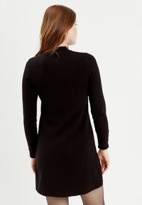 Robe noire à manches longues avec un design simple, fabriquée en tissu doux et texturé, dotée d'un col rond et d'un ourlet légèrement évasé.