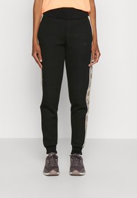 Pantalons de survêtement noirs au design ajusté, avec une taille élastique et des bandes latérales crème contrastantes présentant un motif répété.