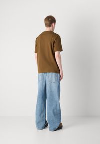 Braunes Baumwoll-T-Shirt und lockere hellblaue Jeans. Das T-Shirt hat einen Rundhalsausschnitt; die Jeans haben große Taschen und ein weites Bein-Design.