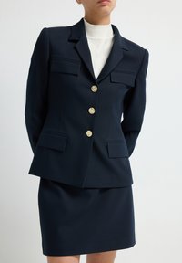 Traje a rayas azul marino que incluye un blazer ajustado con botones dorados y dos bolsillos de parche, combinado con una falda lápiz a juego.