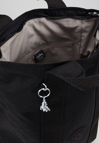 Zwarte draagtas van duurzaam stof, met een beige interieur en een zilveren bedel. Voorzien van een vak met ritssluiting en logodetail.