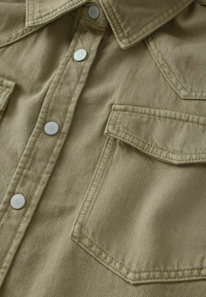 Khaki kauluspaita, joka on valmistettu teksturoidusta kankaasta ja jossa on viistot kaulus, kaksi rintataskua, hopeanväriset napit sekä näkyvät ompeluyksityiskohdat.
