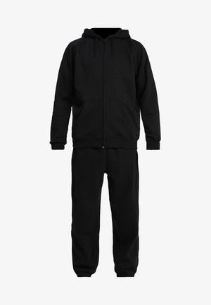 Felpa nera con zip dal tessuto morbido e polsini a coste, abbinata a pantaloni jogger neri con vita elastica.