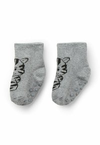 Un paio di calzini per neonati grigi con un design di faccia di gatto nero e puntini antiscivolo sulle suole, posizionati piatti su uno sfondo bianco.