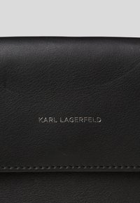 Portefeuille en cuir noir avec une surface texturée, présentant le logo embossé "KARL LAGERFELD" en argent. Surpiqûres régulières le long des bords.
