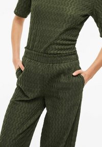 Olijfgroene textuur-outfit met golvend patroon; korte mouwen, elastische tailleband en zijzakken op de losvallende broek.