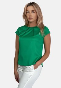 Zielony krótko rękawowy top z okrągłym dekoltem i plisowanym przodem; w połączeniu z białymi dopasowanymi spodniami. Gładki materiał, casualowy krój.