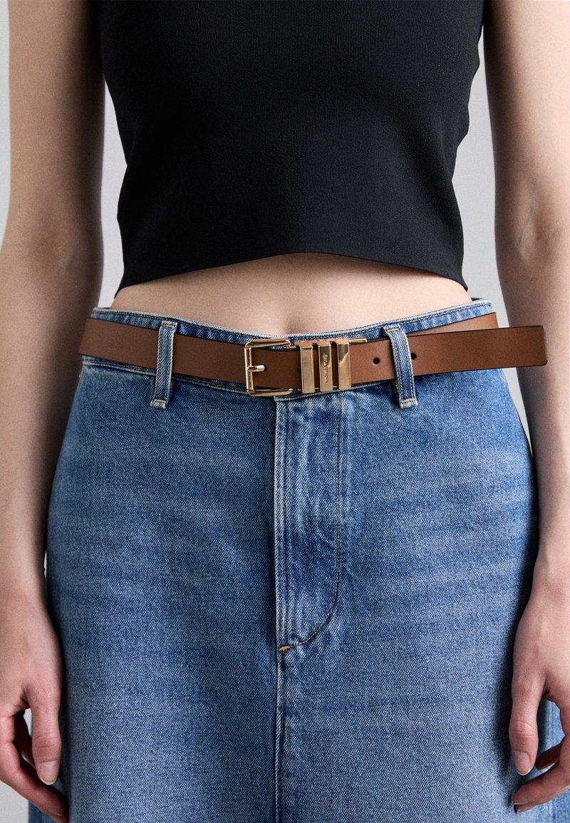 Cintura in pelle marrone con una fibbia in metallo dorato, indossata su jeans azzurri chiari, con vita alta e taglio dritto.