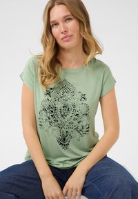 T-shirt vert à manches courtes avec un design mandala noir complexe. Tissu doux, coupe décontractée et encolure ronde.