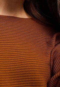 Brun ribbad topp med horisontella ränder, med en mjuk textur och lätt drapering vid axeln, som framhäver en figurnära design.