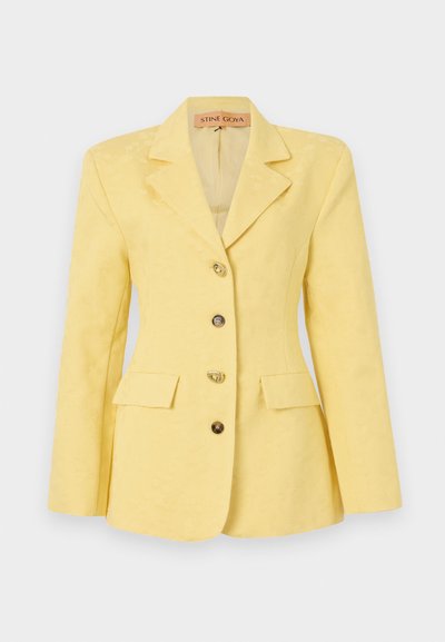 Dzeltena žakete ar rakstu, ar izgrieztu apkakli, viena rinda pogu, trim priekšējiem kabatām un zeltītām pogām. Gluda auduma tekstūra.