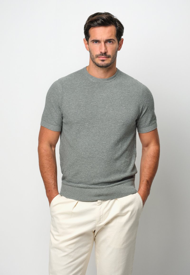 Grå kortärmad stickad tröja med rund halsringning och ribbad nederkant, i kombination med krämfärgade byxor i avslappnad passform.