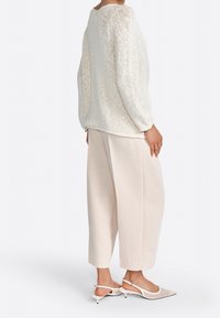 Suéter blanco de punto con corte holgado, que presenta un escote redondeado. Combinado con pantalones de crema de cintura alta y tacones de slingback con punta.