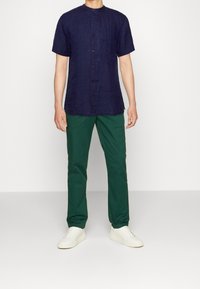 Navy linen short-sleeve shirt with a stand collar and front buttons, paired with green chinos and white sneakers.