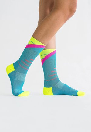Mehrfarbige Socken haben eine türkisfarbene Basis mit leuchtend gelben Zehen und Fersen. Auffällige rosa und gelbe Streifen erzeugen ein dynamisches Muster.