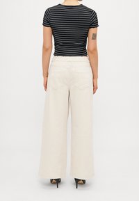 Top de manga corta a rayas en blanco y negro, combinado con pantalones anchos color crema, que cuentan con una cinturilla elástica y dos bolsillos traseros.