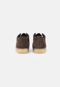 Chaussures en daim marron avec un profil bas, une forme arrondie et des semelles en caoutchouc léger. Elles sont dotées de deux languettes à l'arrière pour un enfilage facile.