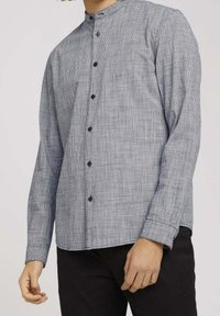 Camisa de manga larga con botones en un patrón de cuadros en blanco y negro, con cuello alto y botones oscuros. La artesanía muestra una textura fina.