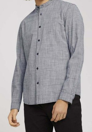Camisa de manga larga con botones en un patrón de cuadros en blanco y negro, con cuello alto y botones oscuros. La artesanía muestra una textura fina.