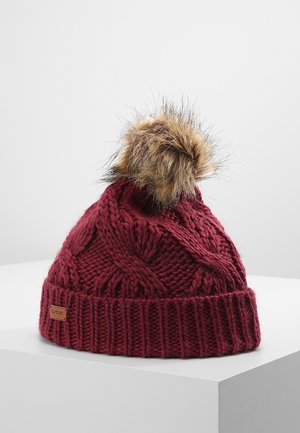 Bonnet bordeaux en maille torsadée, avec un revers côtelé, une étiquette Barbour beige et un pompon marron en fausse fourrure, présenté sur un socle blanc.