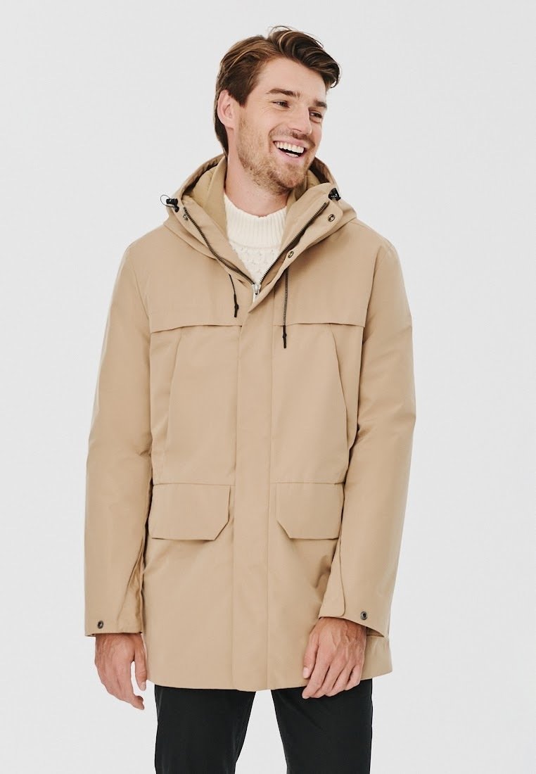 Beżowa wodoodporna parka z kapturem, z zamkiem błyskawicznym z przodu, dwoma dużymi kieszeniami z przodu, regulowanymi sznurkami i gładką teksturą.
