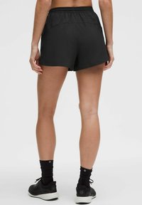 Zwarte sportieve shorts met een elastische tailleband, lichtgewicht stof en een losse pasvorm. Draagt met zwarte sneakers en enkelsokken.